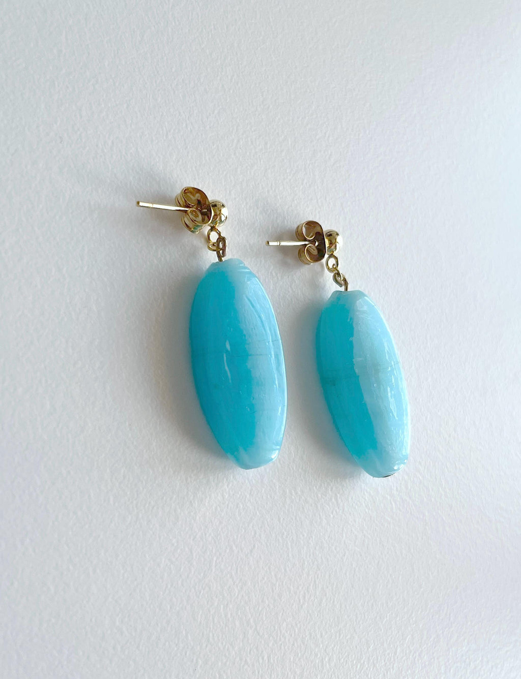 A pair of drop earrings with oval light blue turquoise-like beads suspended from gold-tone posts, shown on a plain white background.