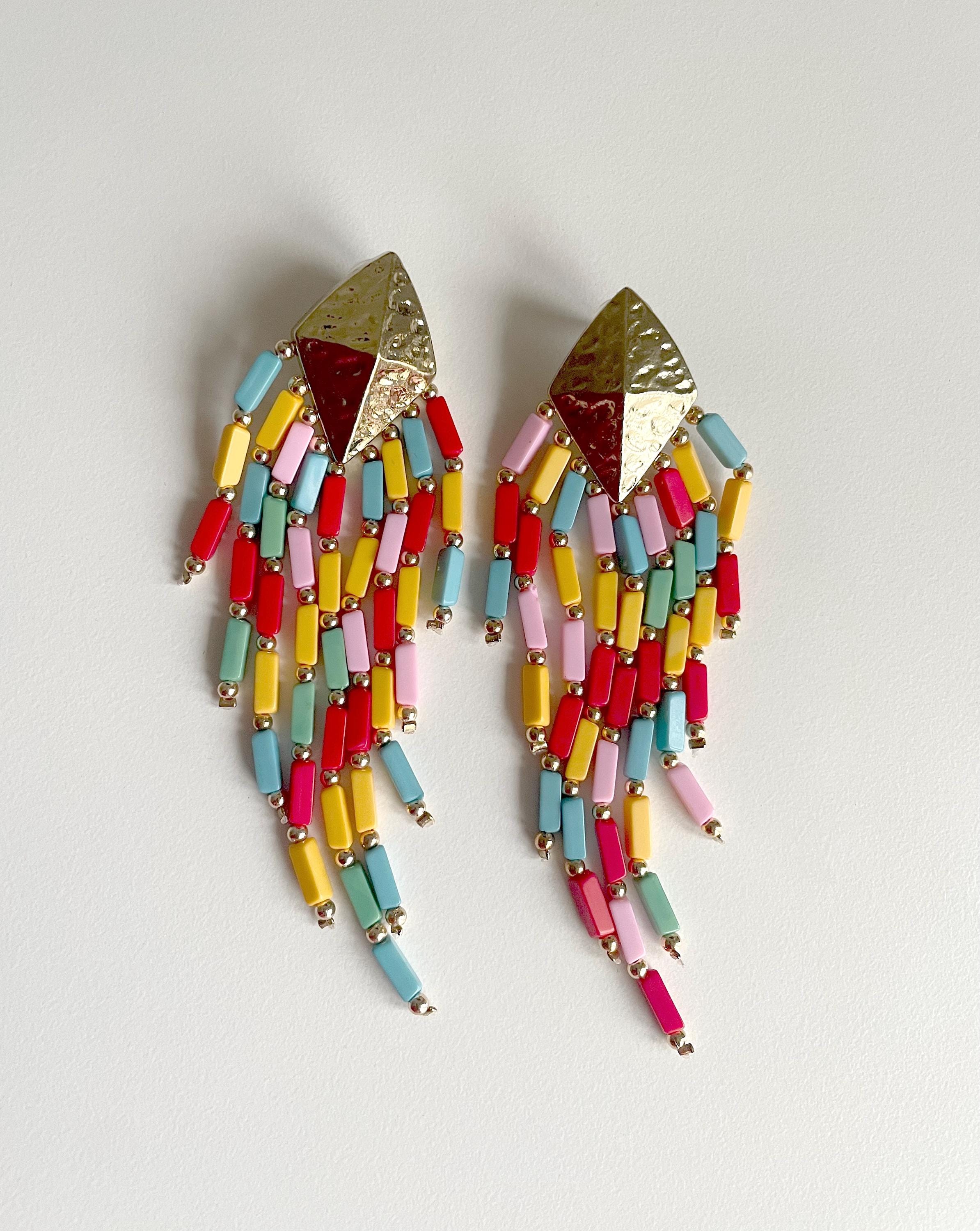 A pair of colorful beaded dangle earrings with textured gold-tone triangular studs and cascading cylindrical beads in pink, red, yellow, light blue, and mint on a plain light background.