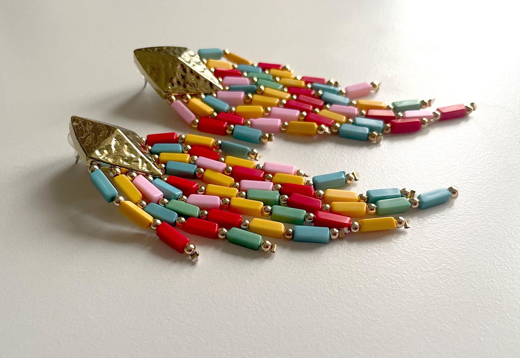 A pair of dangling statement earrings with textured gold-tone triangular studs and cascading rows of small cylindrical beads in red, yellow, pink, light blue, mint green, and orange on a white background.