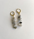 A pair of gold hoop drop earrings with dangling irregular gray, white, and dark charcoal quartz chips, displayed on a clean white textured background.