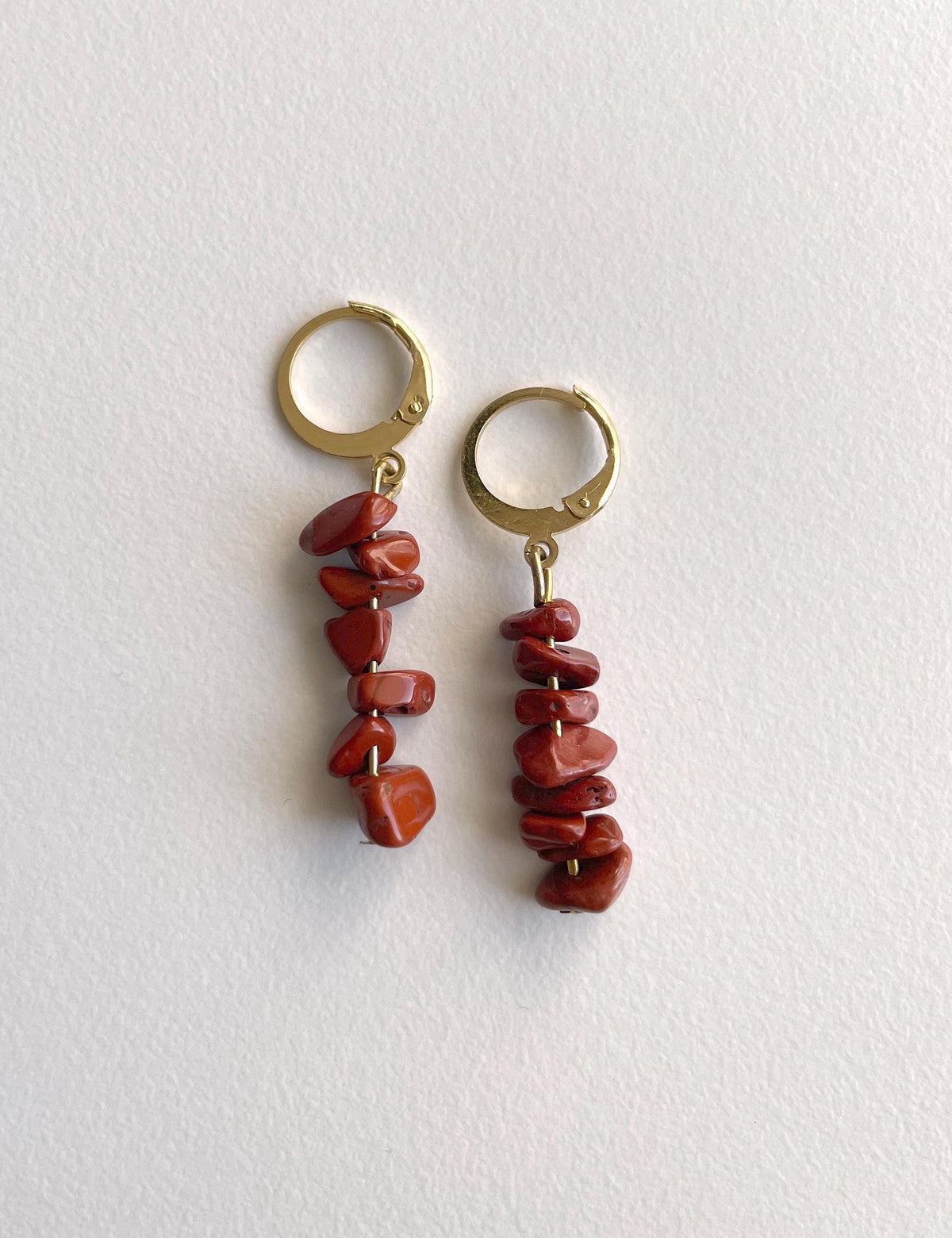 A pair of gold hoop earrings with dangling clusters of polished reddish-brown red jasper stone chips, displayed on a clean white textured background.