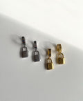 Four small padlock-shaped jewelry charms or earrings in silver and gold finishes, arranged on a plain white surface with soft shadows.