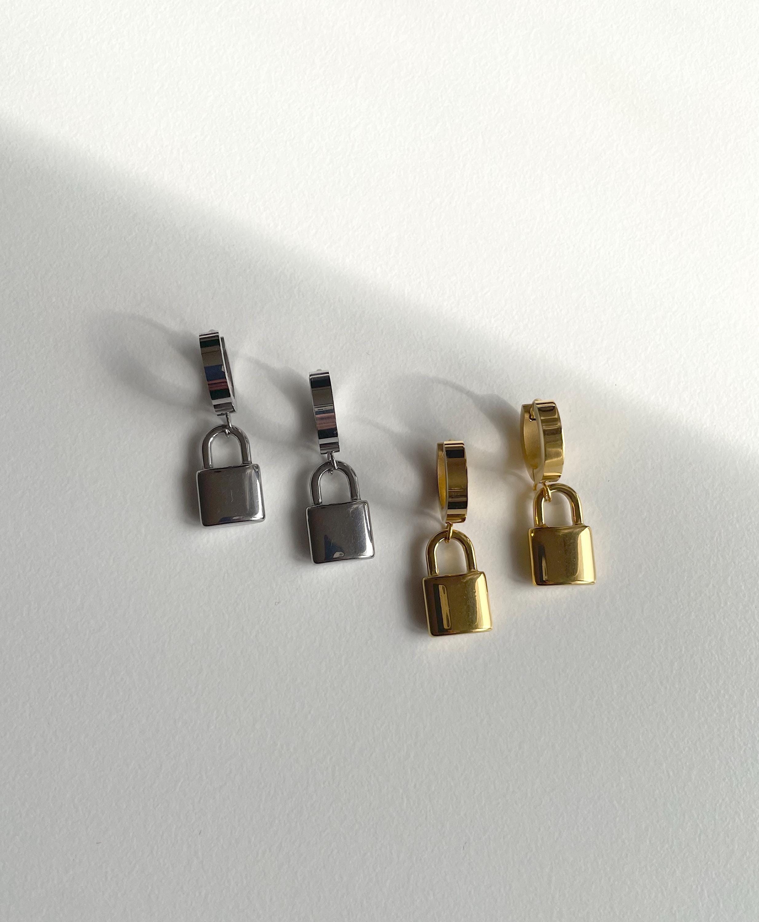 Four small padlock-shaped jewelry charms or earrings in silver and gold finishes, arranged on a plain white surface with soft shadows.