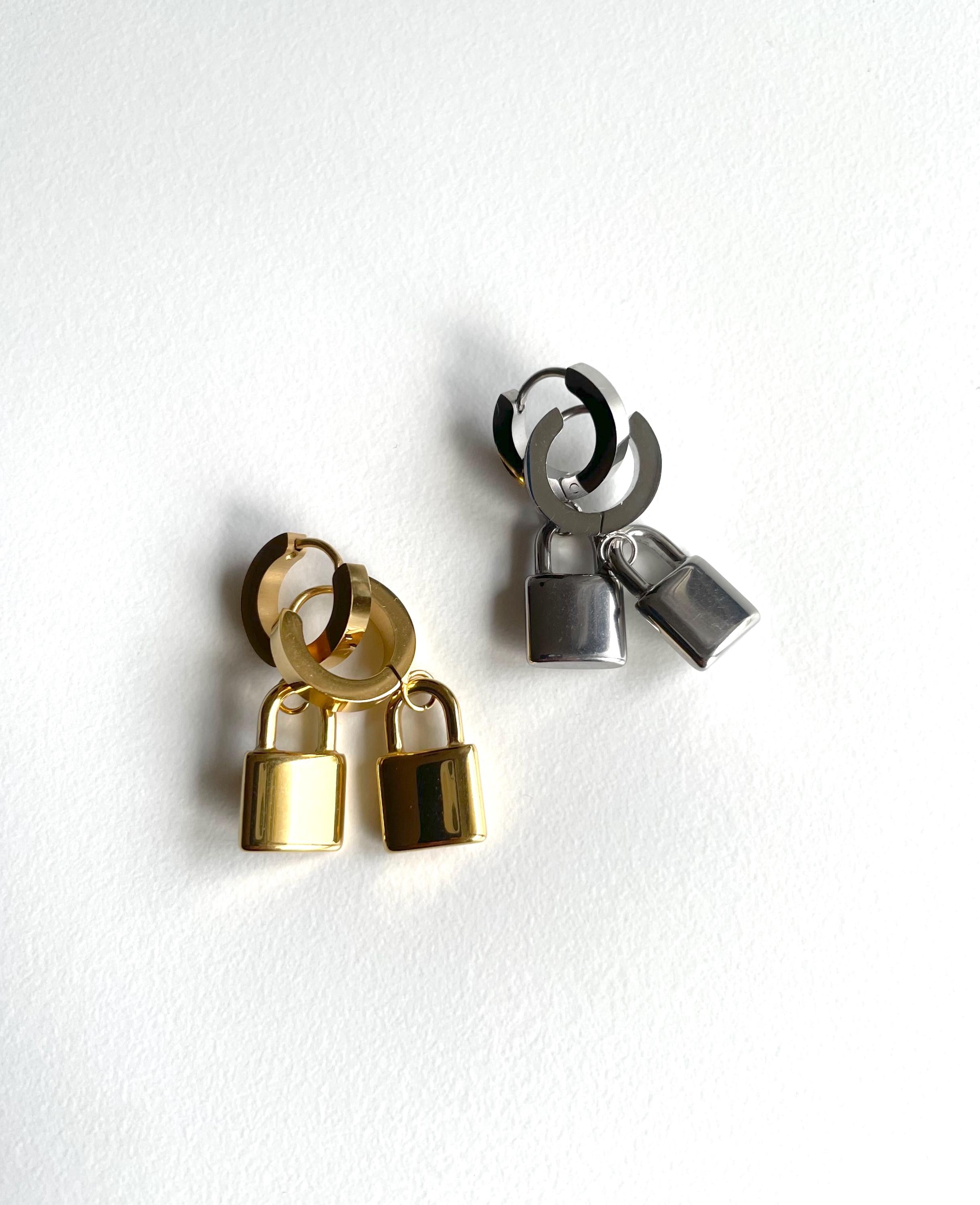 Two pairs of small hoop earrings with dangling padlock charms, one in polished gold and one in polished silver, displayed on a clean white background.