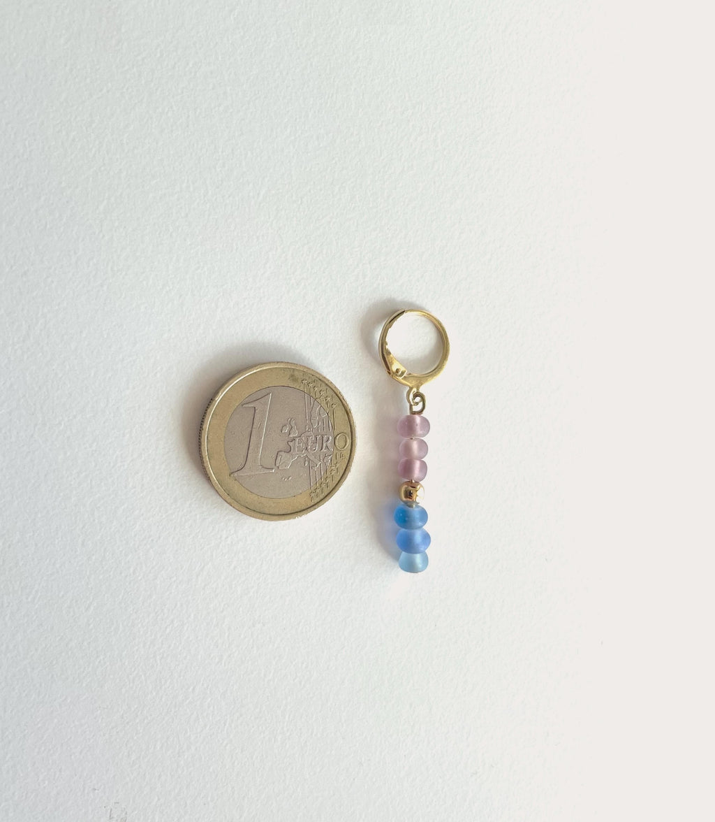 A small gold-tone keyring charm with three beads in light pink and blue, shown next to a 1 Euro coin for scale on a plain white background.