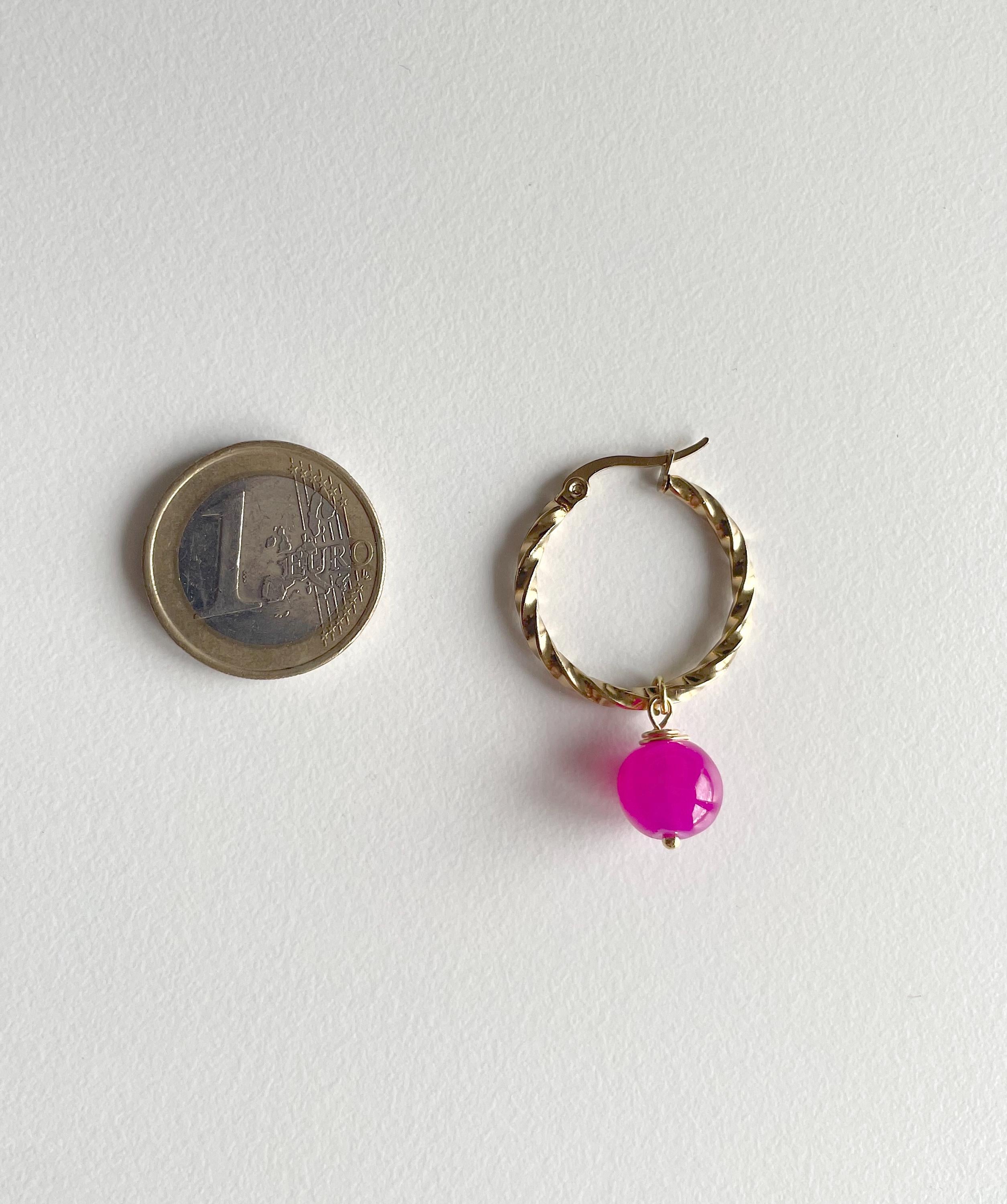 A small gold hoop earring with a dangling bright pink bead, shown next to a euro coin for scale on a plain white background.
