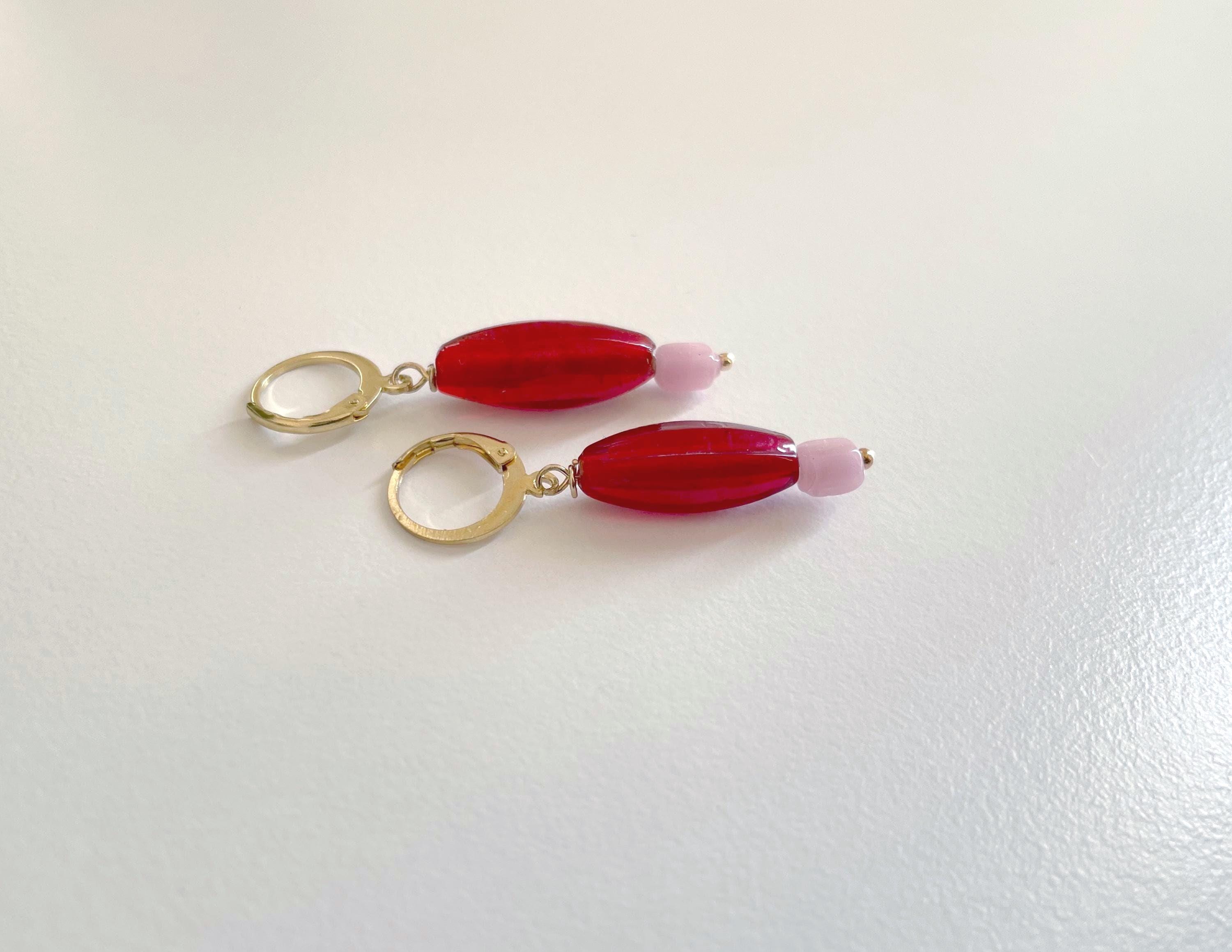 A pair of gold hoop earrings with elongated red beads and small light pink beads, displayed on a plain white surface.