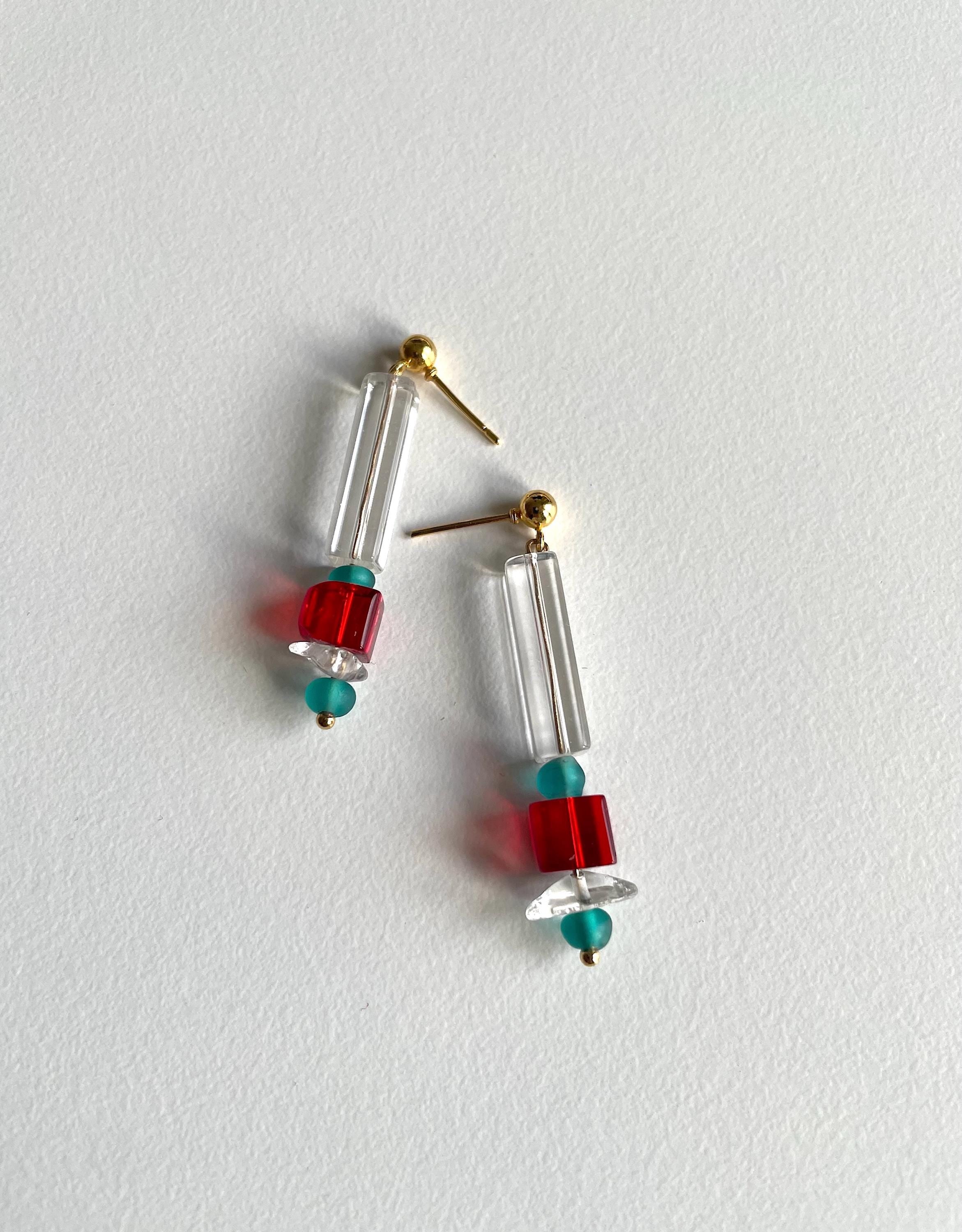 A pair of drop earrings with clear cylindrical beads, red square beads, and small turquoise beads, hanging against a plain white background.
