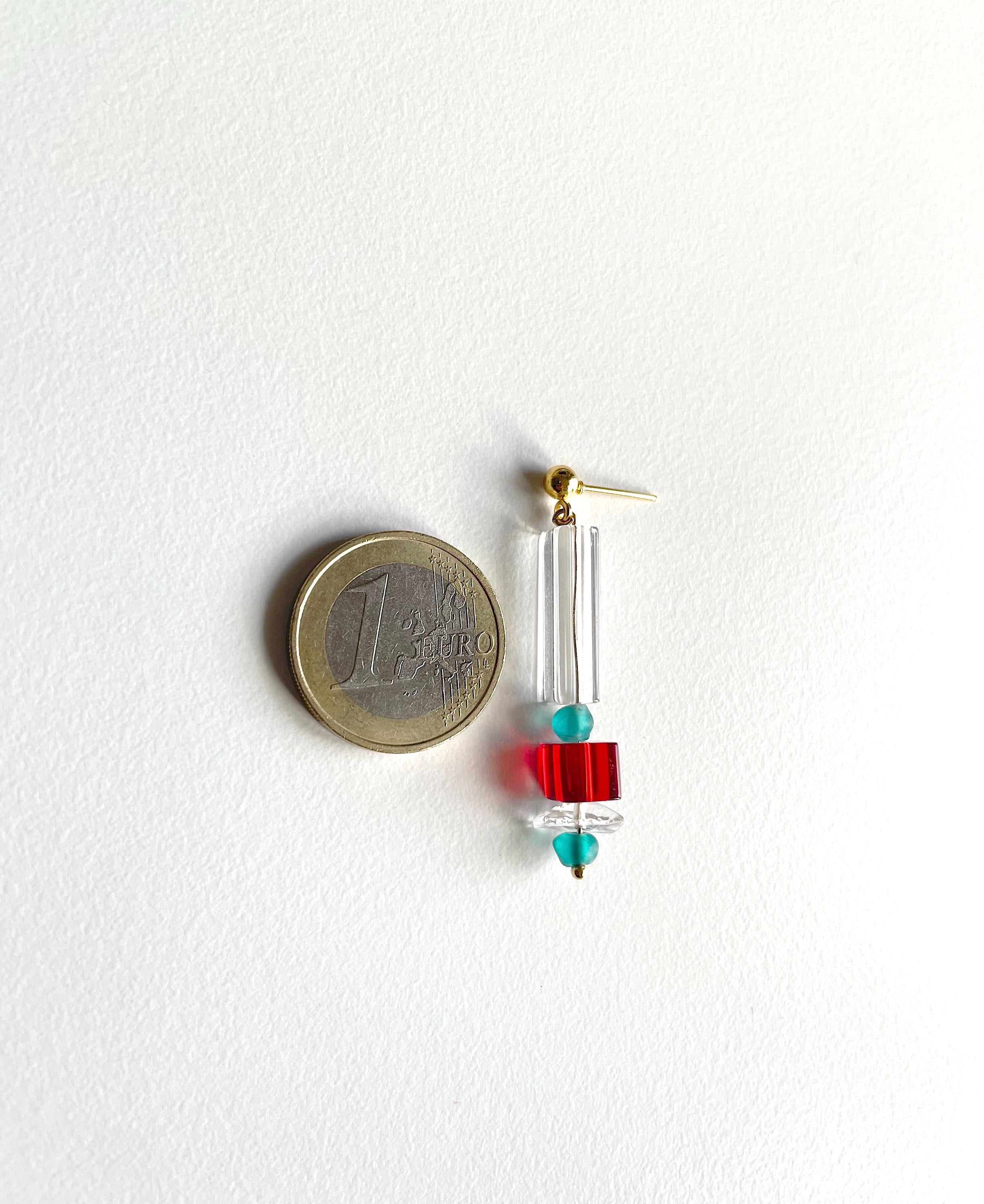 A single drop earring shown next to a 1 Euro coin for scale, featuring a gold-plated fishhook back, clear acrylic tubes, a red cylindrical bead, and turquoise blue faceted beads on a white background.