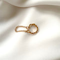 A delicate cuff earring with a textured circular design and a short chain charm extension, displayed on a soft, draped white fabric background.