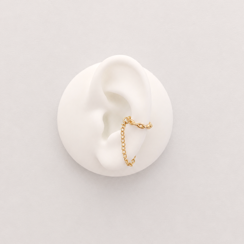A delicate rose gold ear cuff with a small dangling chain charm, displayed on a white ear-shaped mannequin against a light gray background.