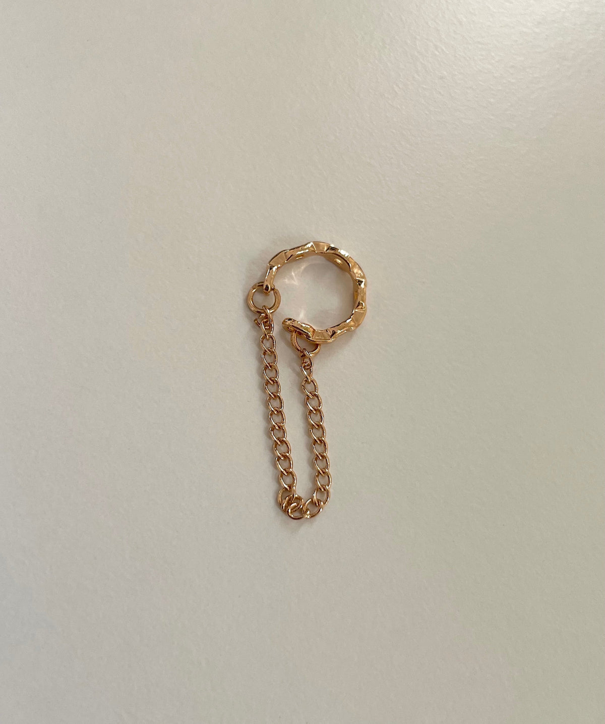 A rose gold cuff earring with a short chain charm extension, photographed on a plain light gray background.
