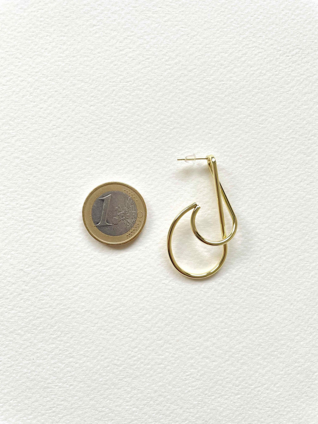 A pair of gold hoop earrings displayed next to a 1 Euro coin on a textured white background.