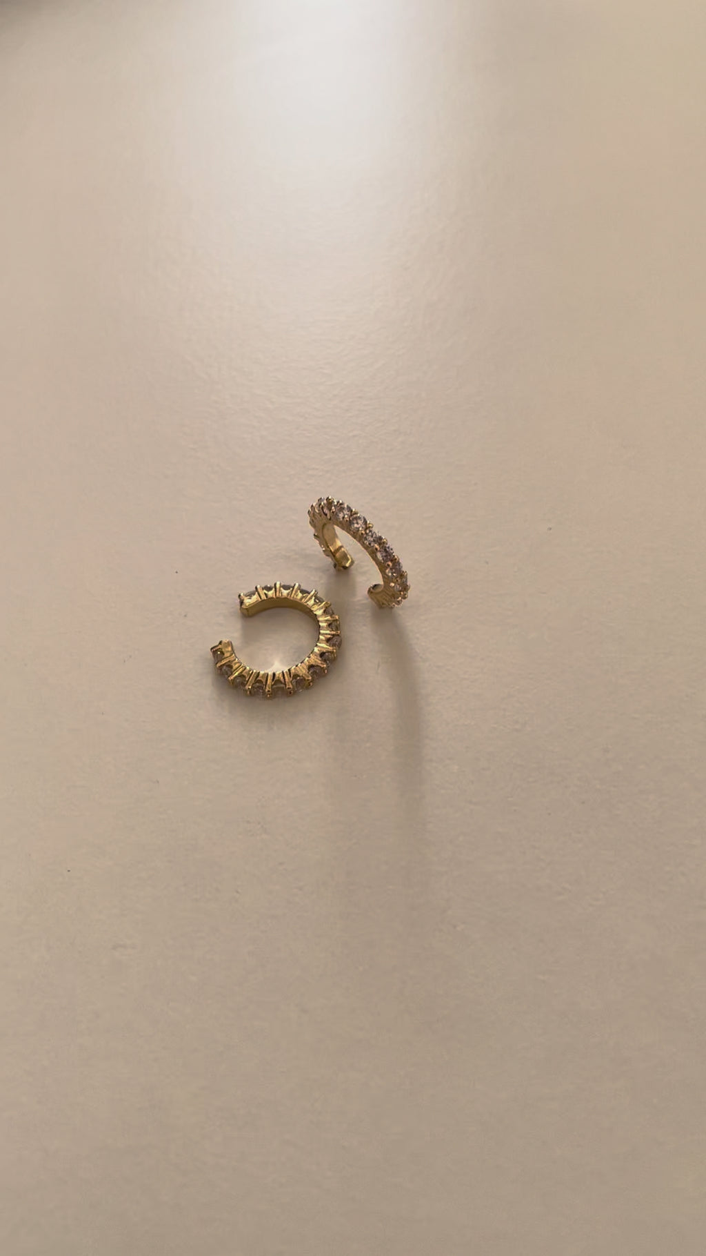 A pair of gold plated crystal cuff earrings with cubic zirconia crystals on a white surface with sunlight making the crystals shine
