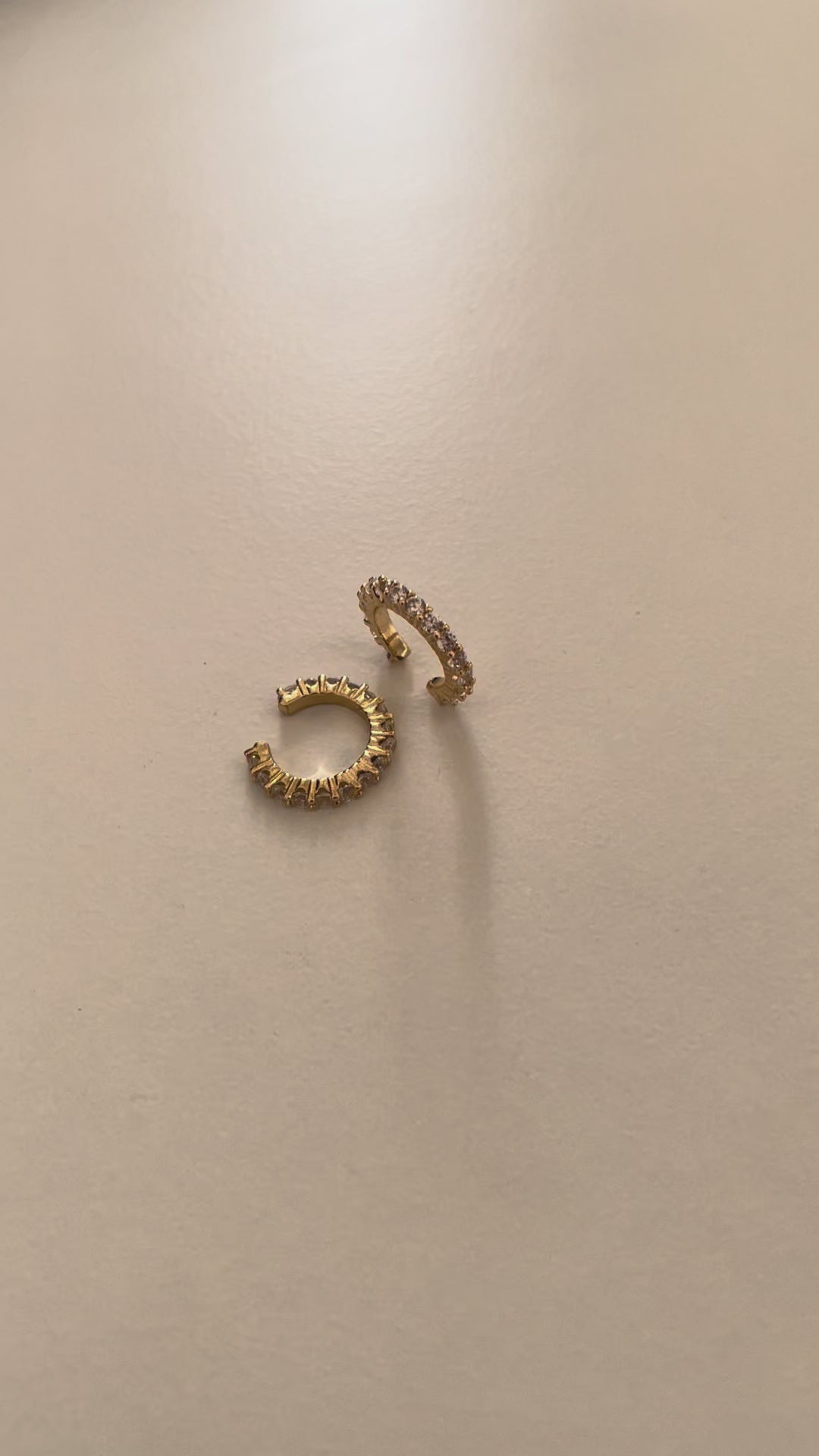 A pair of gold plated crystal cuff earrings with cubic zirconia crystals on a white surface with sunlight making the crystals shine