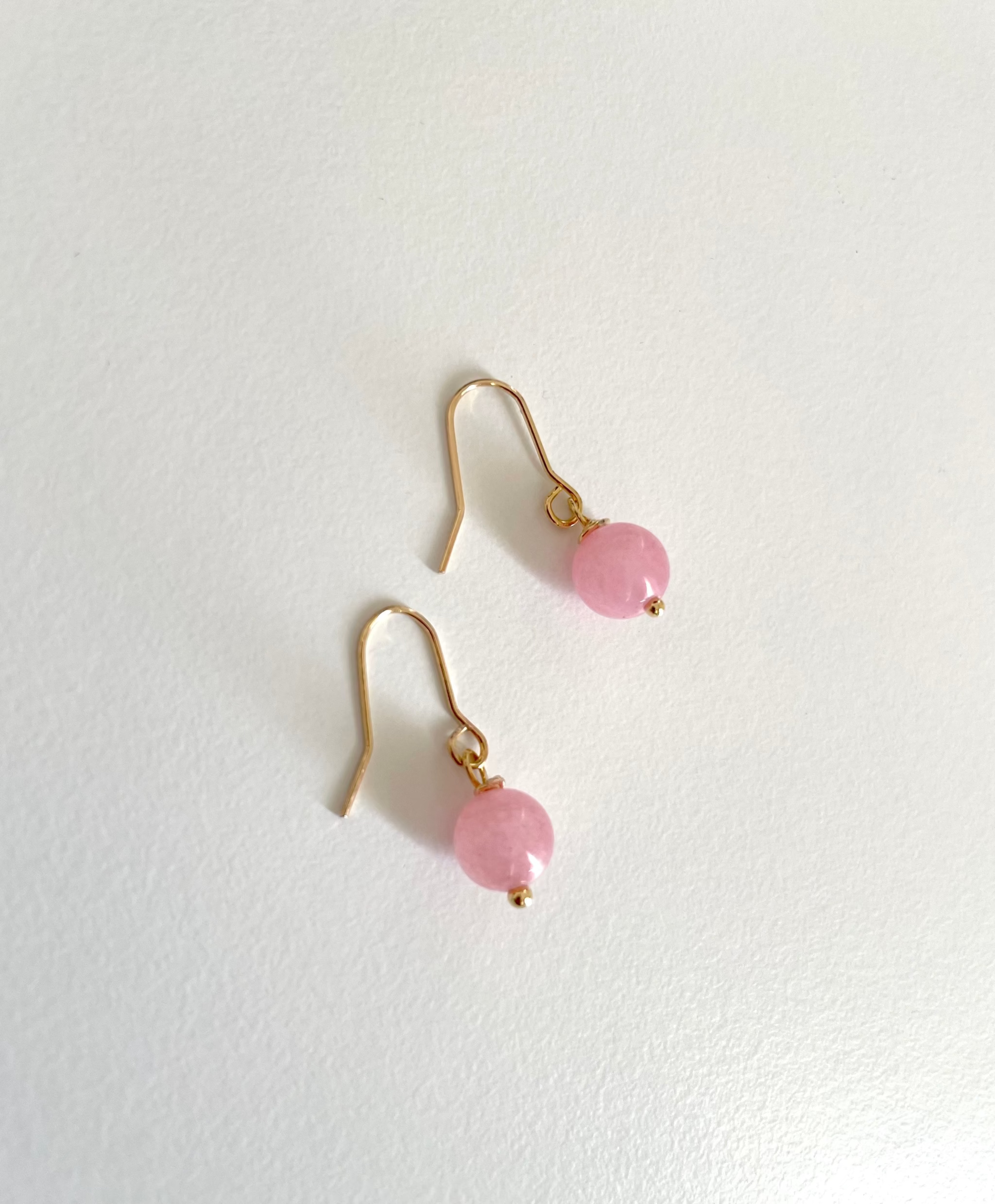A pair of 18k gold plated fishhook earrings with small round pastel pink bead drops made of real rose quartz beads, displayed on a clean white textured background.